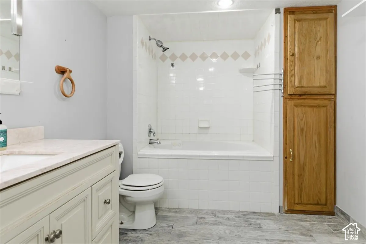 Bathroom featuring a built-in tub with shower, a vanity with an integrated sink and stone-finish countertop, wood-finish flooring, and a full-height wood-finish storage cabinet