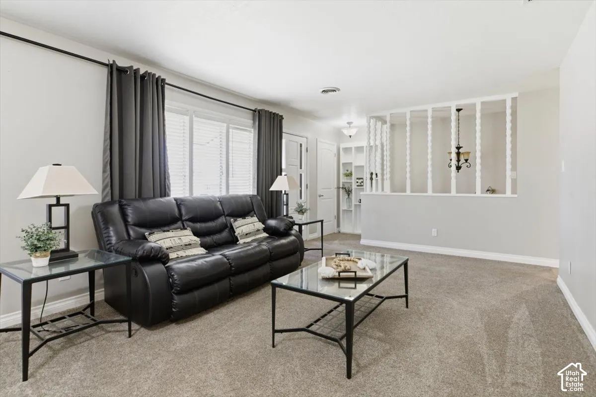 Bright living area featuring light-toned walls, carpet flooring, a large window with blinds, and white decorative half-wall detailing