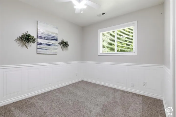 Spacious room featuring panel wainscoting, light grey wall paint, and plush carpet flooring