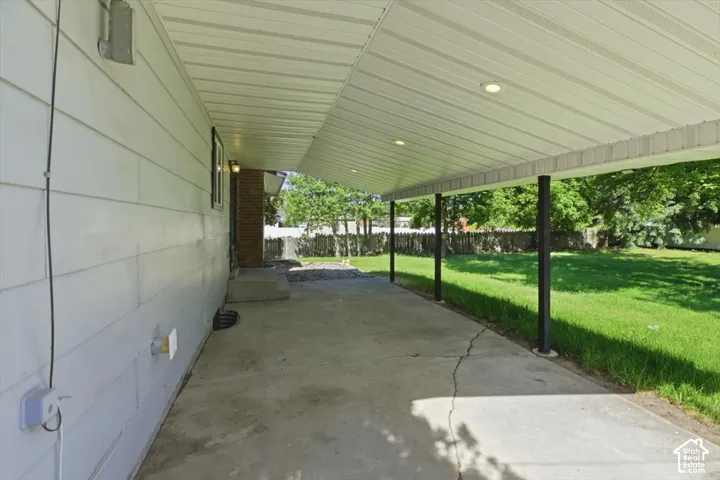 Covered concrete patio extending along the home's siding, featuring recessed lighting and support columns