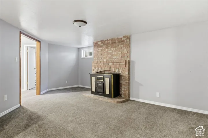 Carpeted room featuring a brick fireplace surround with an inset wood-burning stove