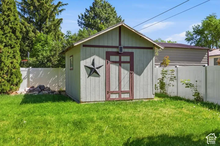 Detached storage shed with light-colored siding and dark trim, featuring a single window and a decorative star accent
