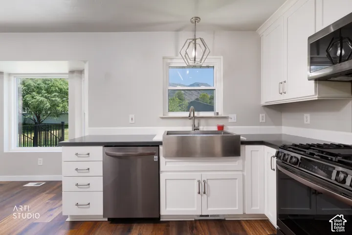 Modern kitchen featuring white cabinetry with brushed nickel hardware, dark countertops, a stainless steel farm sink with a gooseneck faucet, a stainless steel dishwasher, and a gas range