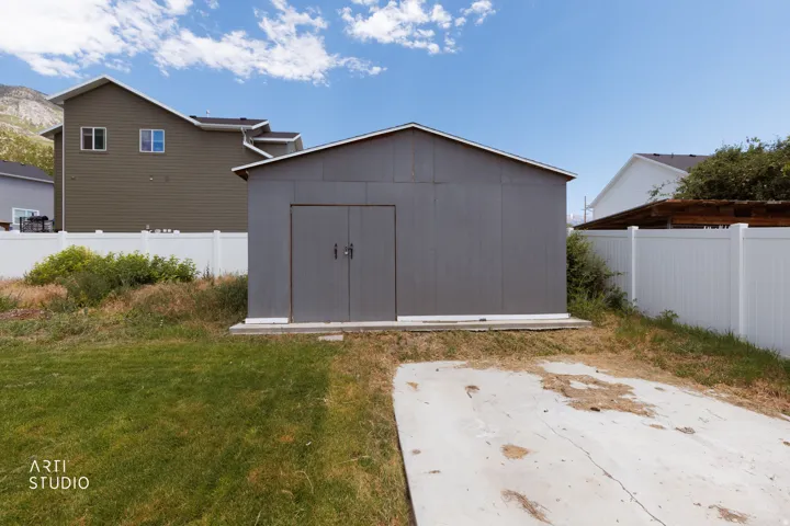 Detached storage shed featuring a metal exterior and double doors, positioned on a concrete pad