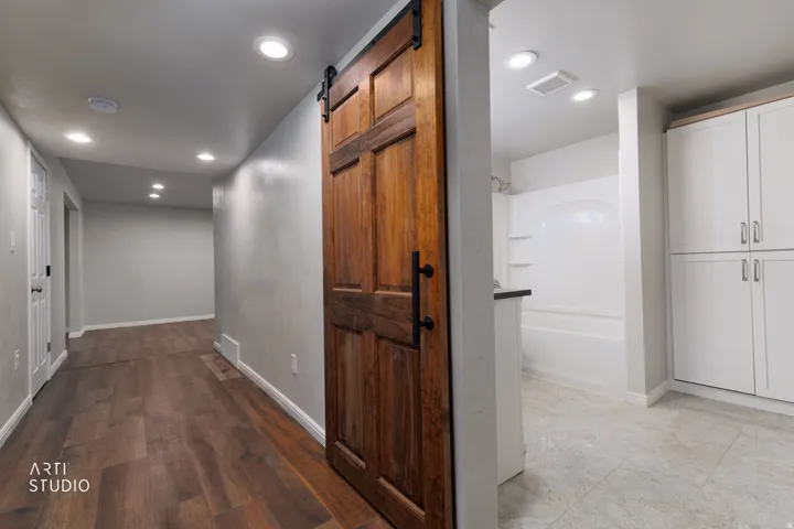 Rustic barn door entry to a bathroom featuring a white tub/shower combination, white cabinetry, and recessed lighting