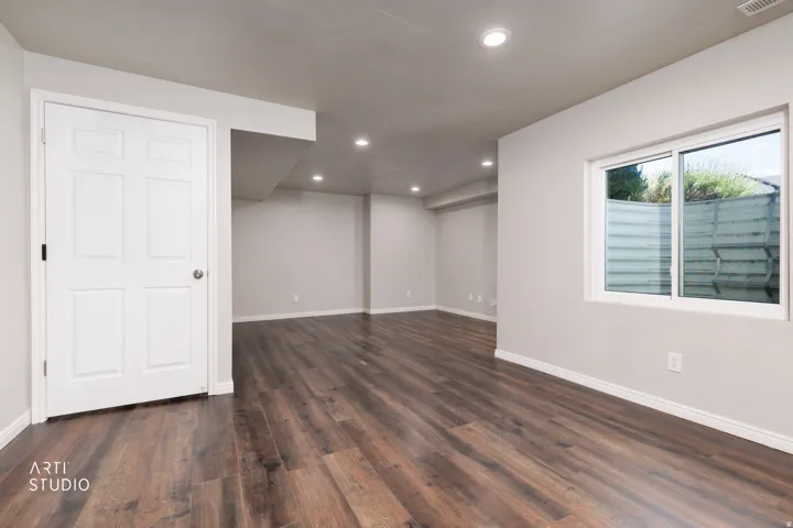 Spacious room featuring wood-finish flooring, recessed lighting, a white six-panel interior door, a sliding window, and neutral wall tones