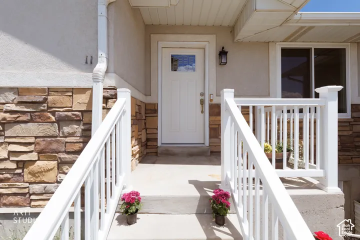 Entryway featuring a white paneled door with a rectangular window, stone veneer siding, stucco finish, white railing, and exterior lighting