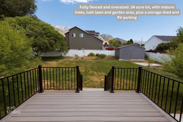 Expansive backyard featuring a composite deck with black metal railings, a large lawn, mature trees, and a storage shed