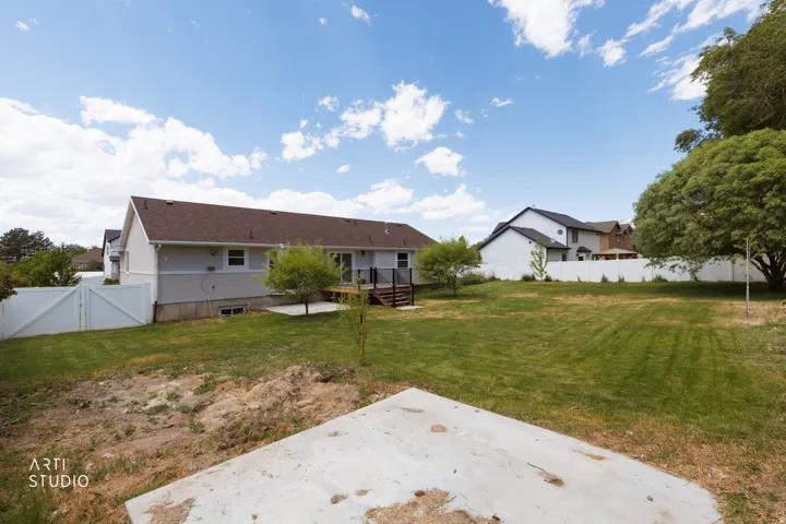 Expansive rear yard featuring a large concrete patio, a wood-finish deck, and a white privacy fence
