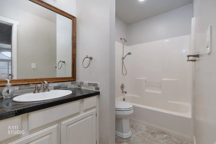 Bathroom featuring a white vanity with a dark countertop, mosaic tile backsplash, and a framed mirror