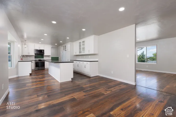 Kitchen featuring wood-finish flooring, white cabinetry, black countertops, and a central island