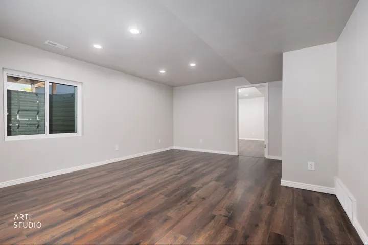 Spacious interior room featuring wood-finish flooring, recessed lighting, a sliding window with exterior view, and crisp white walls