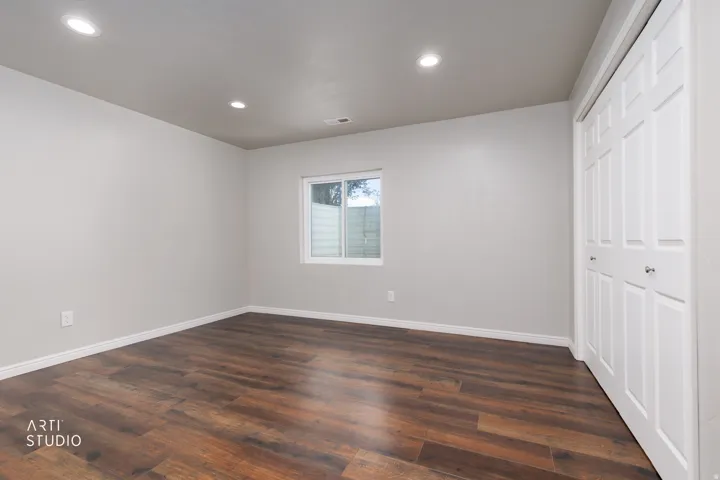 Spacious room featuring wood-finish flooring, recessed lighting, a white framed window, and bi-fold closet doors