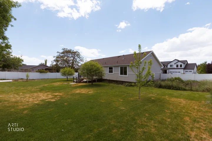 Spacious backyard featuring a substantial lawn, a multi-level wooden deck, mature trees, and a white privacy fence