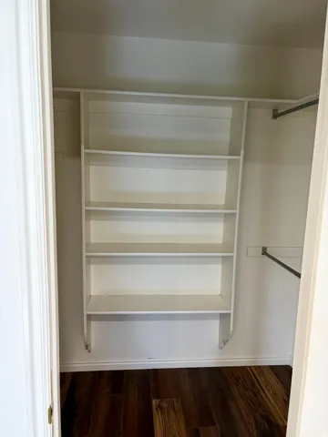 Recessed closet with dark wood-finish flooring, white baseboards, and built-in white shelving