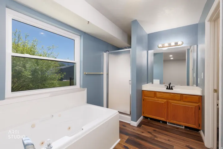 Full bathroom featuring a window above a built-in tub, a glass-enclosed shower, a wood-finish vanity with an integrated sink, and wood-finish flooring