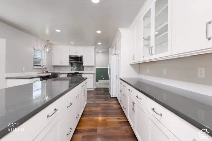 Modern kitchen featuring an expansive island with a dark countertop, white shaker-style cabinetry, wood-finish flooring, recessed lighting, and a stainless steel dishwasher