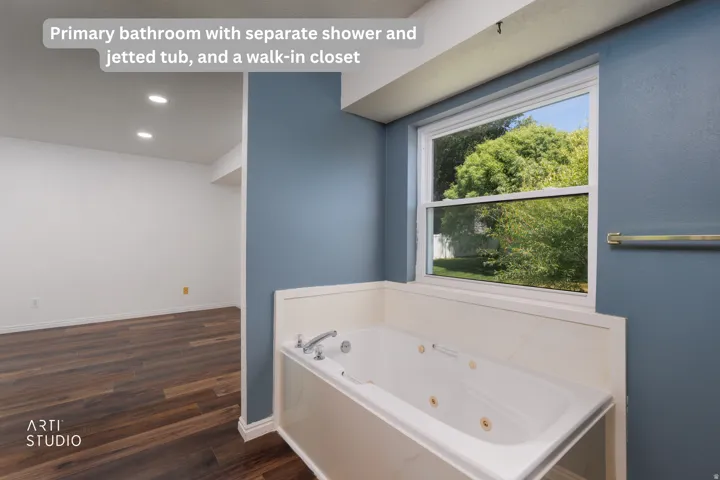 Deep soaking jetted tub with tiled surround, framed window, and rich wood-finish flooring