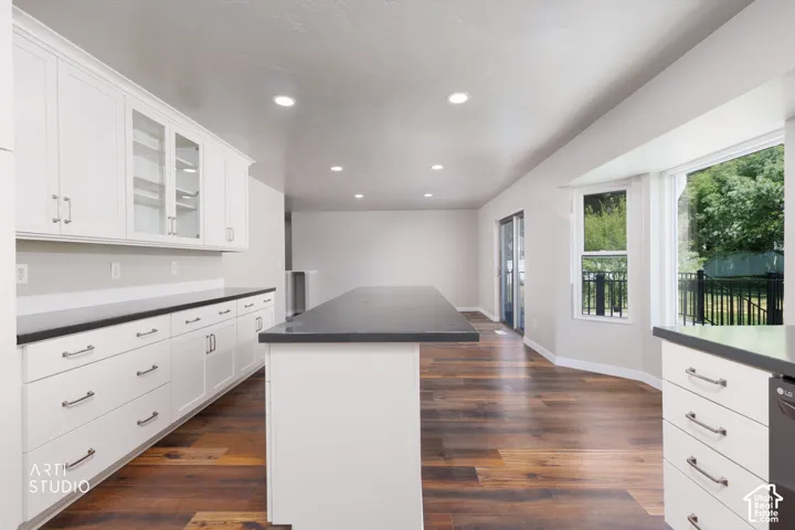 Open-concept kitchen featuring white cabinetry, dark countertops, a central island, wood-finish flooring, and recessed lighting