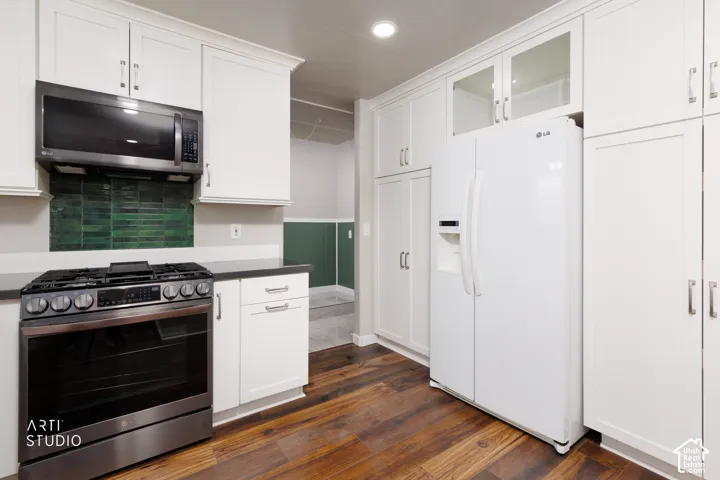 Modern kitchen featuring white shaker cabinetry, dark countertops, a green subway tile backsplash, stainless steel range with microwave, and wood-finish flooring