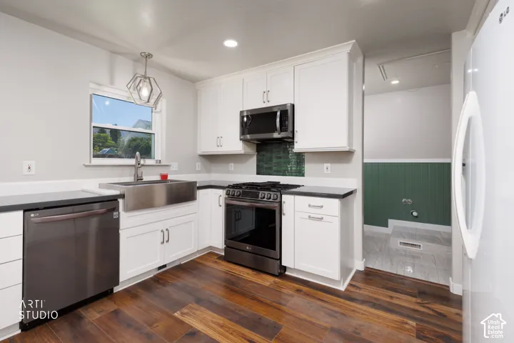 Kitchen featuring wood-finish flooring, white cabinetry with contemporary hardware, stainless steel farmhouse sink, and dark countertops