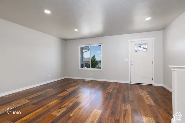 Spacious room featuring rich wood-finish flooring, recessed lighting, and a white entry door with decorative glass inlay