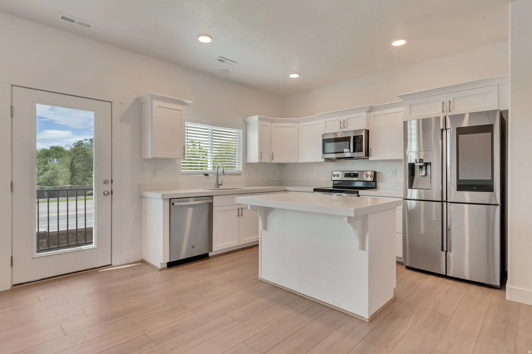 Modern kitchen featuring light wood-finish flooring, white cabinetry with crown molding, stainless steel appliances, a central island, and recessed lighting