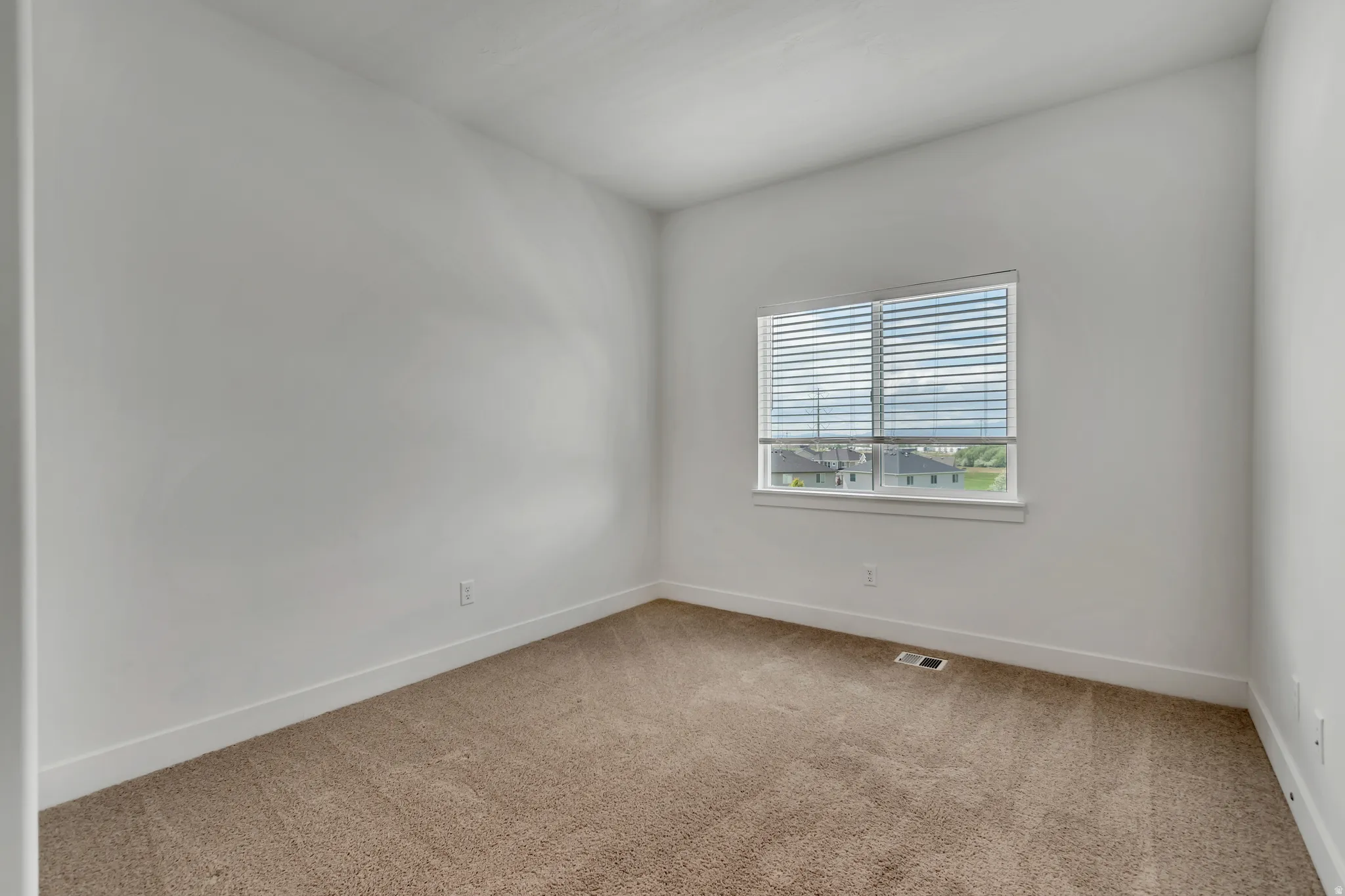 Carpeted room with white walls, a single window featuring horizontal blinds, and white baseboards