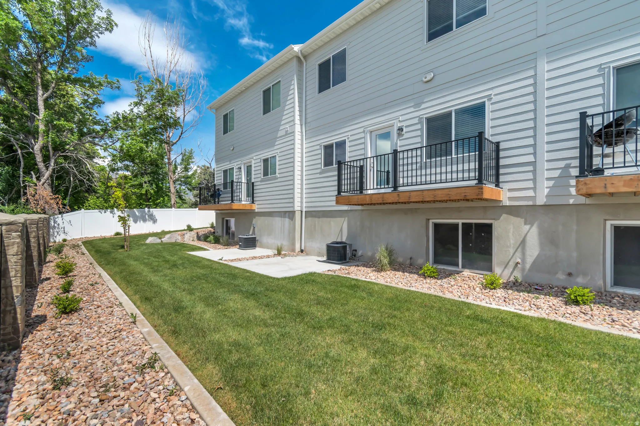 Rear exterior featuring light grey siding, multiple balconies with black railings, and a concrete patio