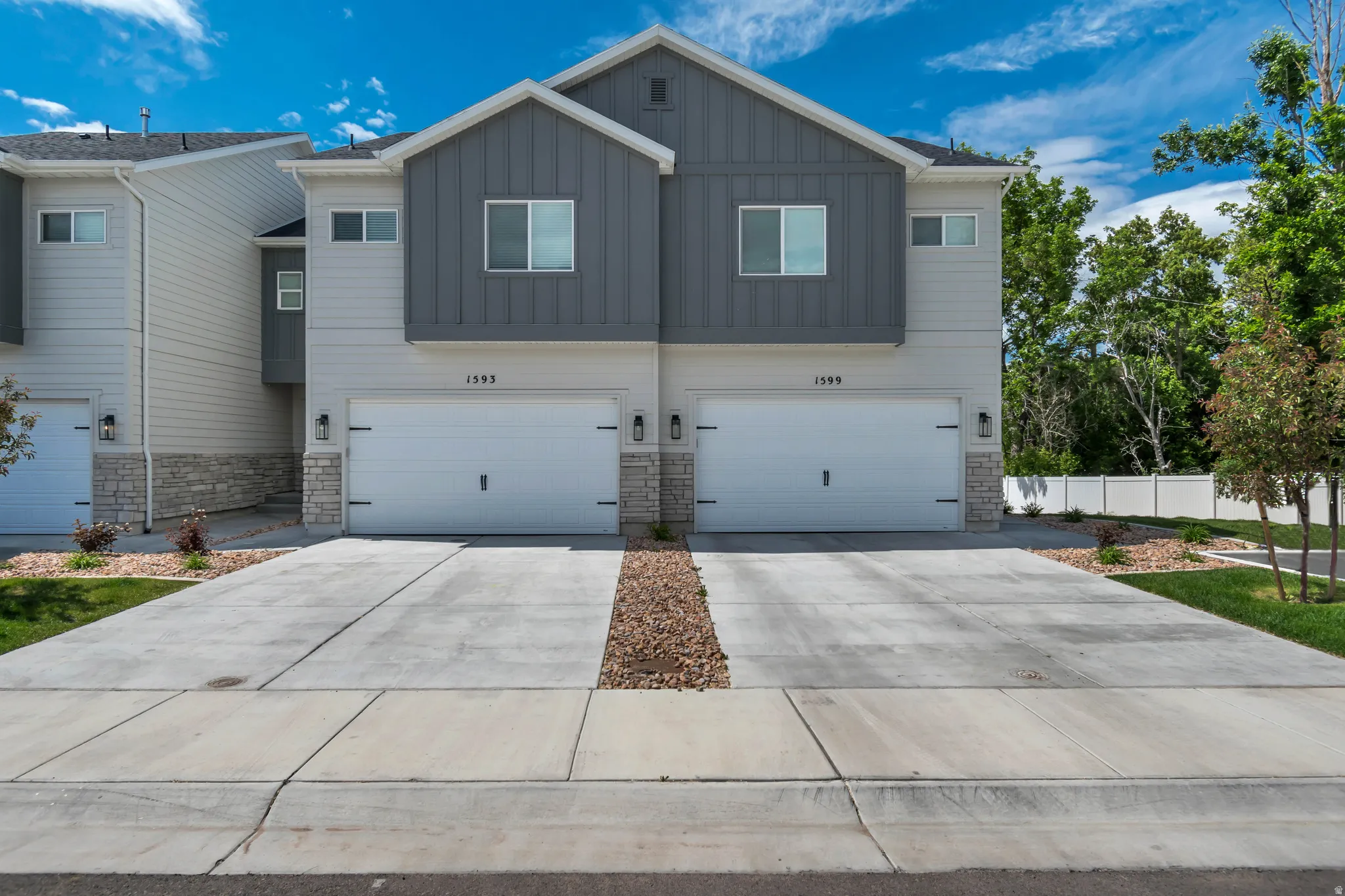 Modern townhome facade featuring light grey siding, vertical dark grey paneling, and stone accents