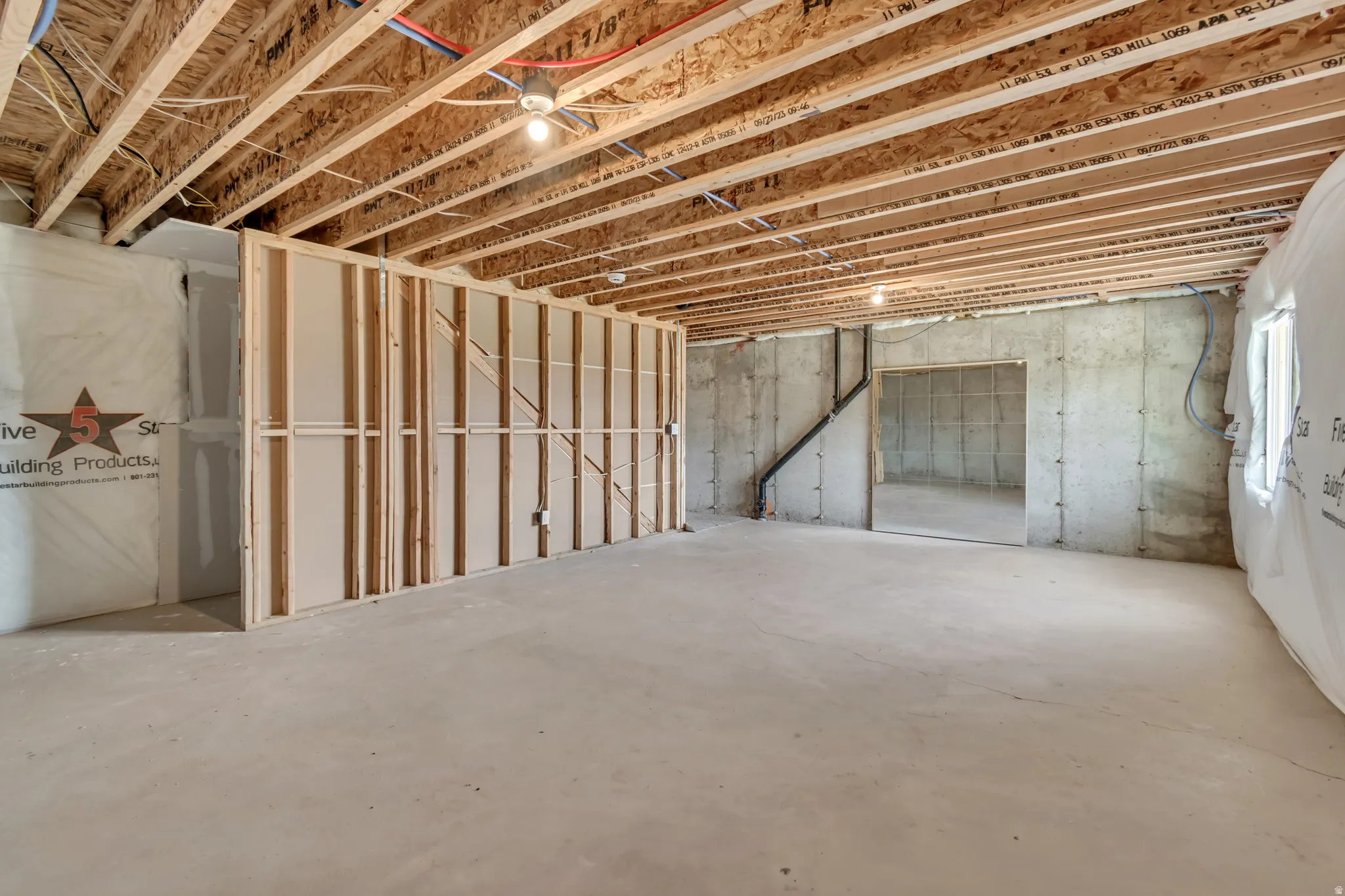 Unfinished basement presenting exposed ceiling joists, concrete flooring, and partial wood framing for future customization
