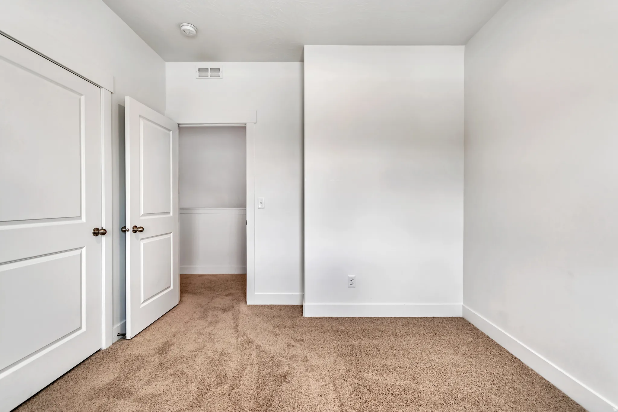 Light-toned wall-to-wall carpeting in a neutral room with white walls and trim