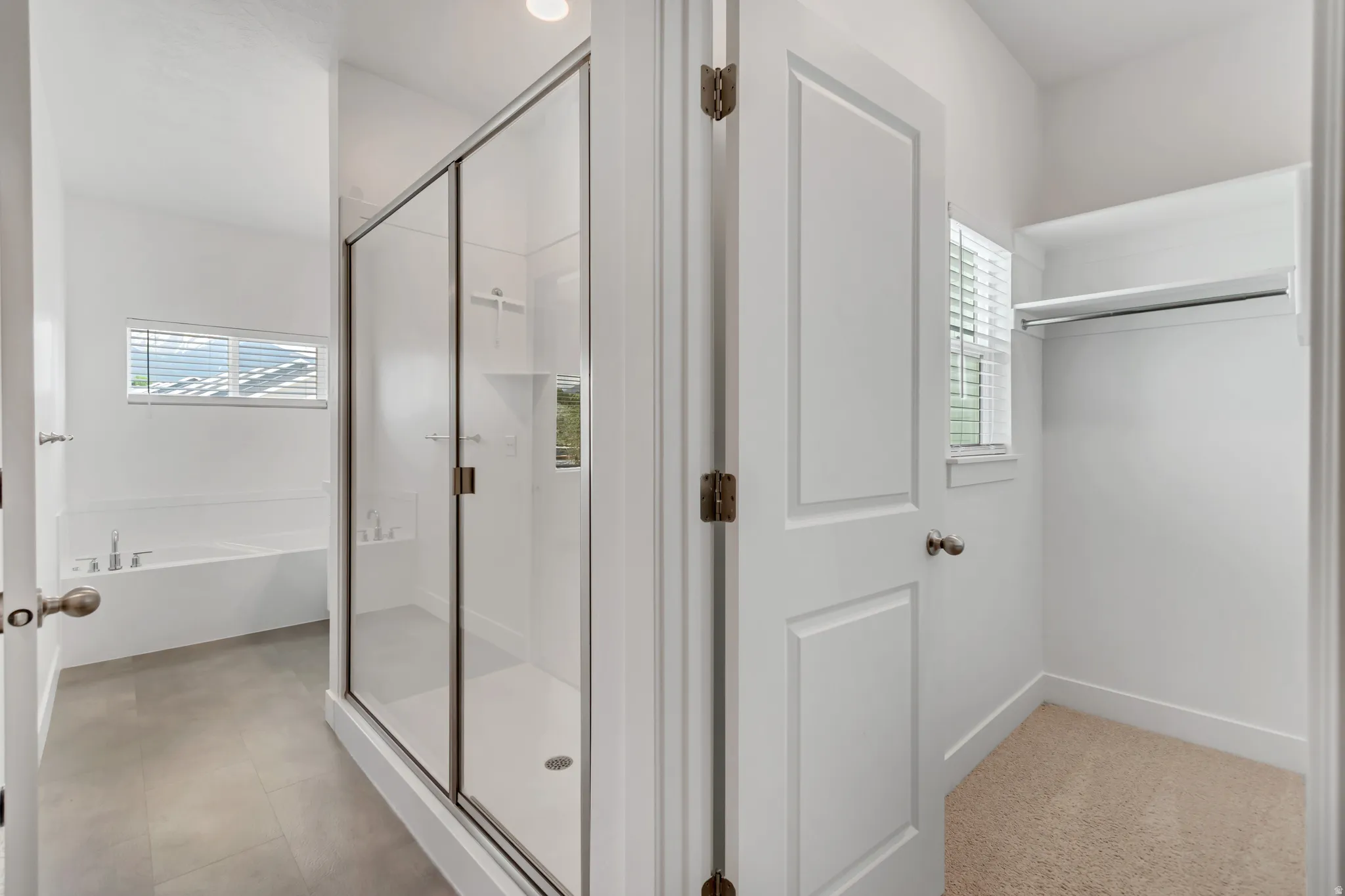 Modern bathroom featuring a glass-enclosed shower with sliding doors, a built-in bathtub, and neutral-toned tile flooring