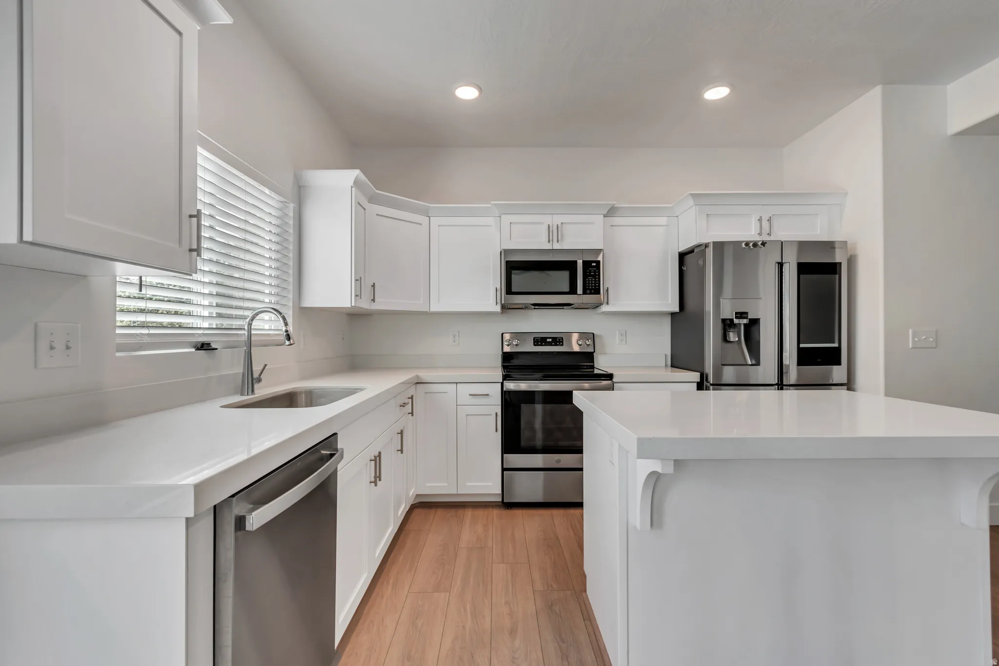 Contemporary kitchen featuring white cabinetry, light-toned countertops, stainless steel appliances, and wood-finish flooring