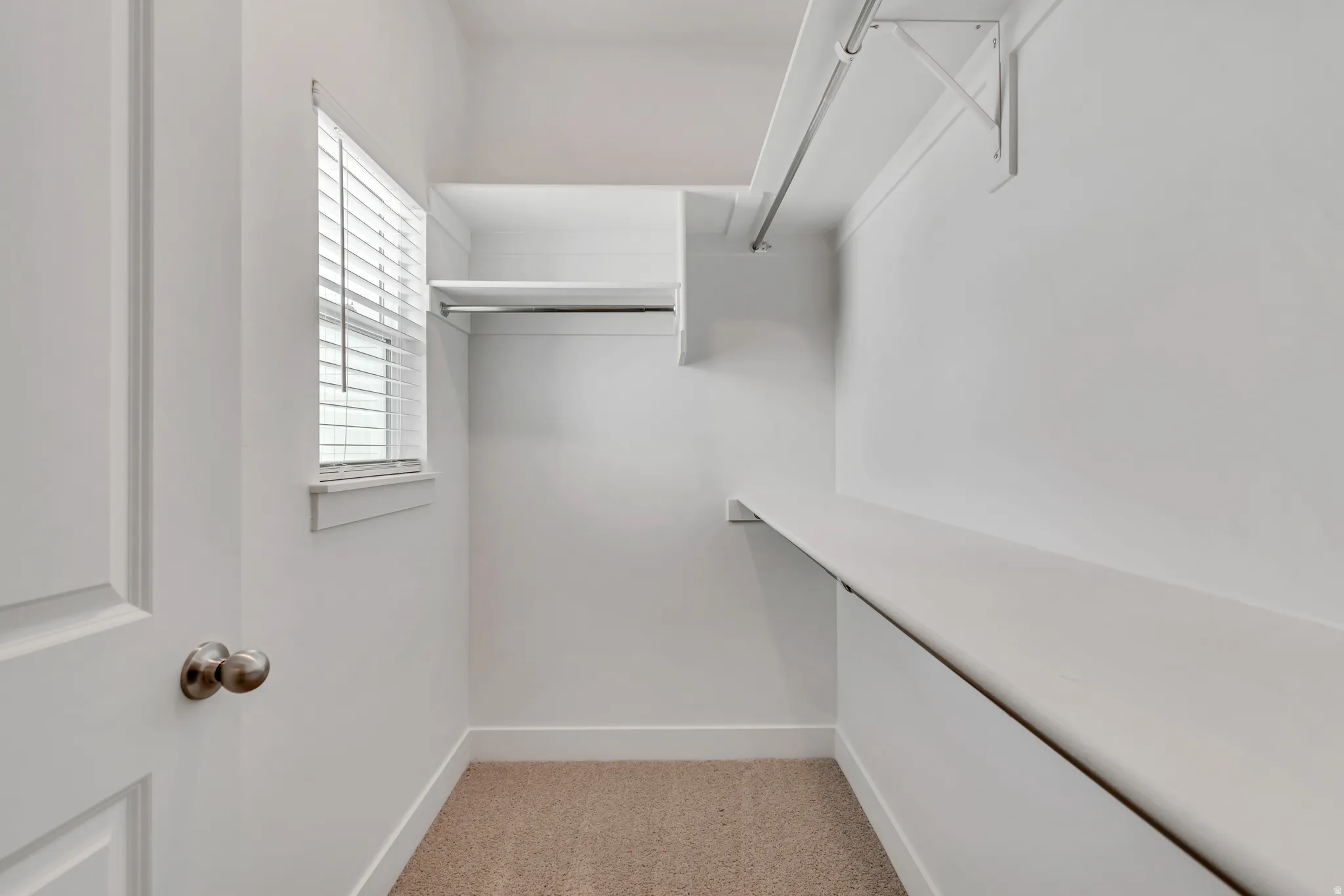 Walk-in closet featuring built-in shelving, hanging rods, and a window with blinds
