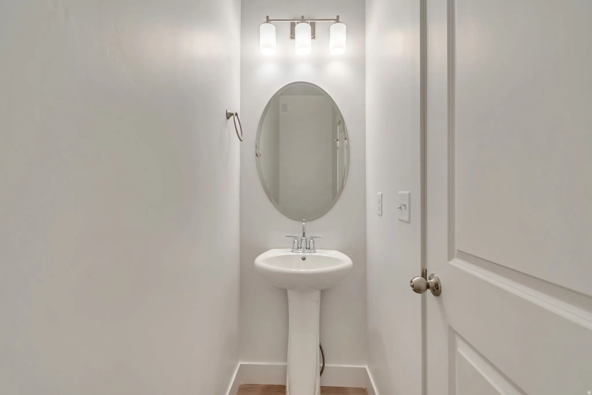 Pedestal sink with chrome faucet, an oval mirror, and a three-light vanity fixture