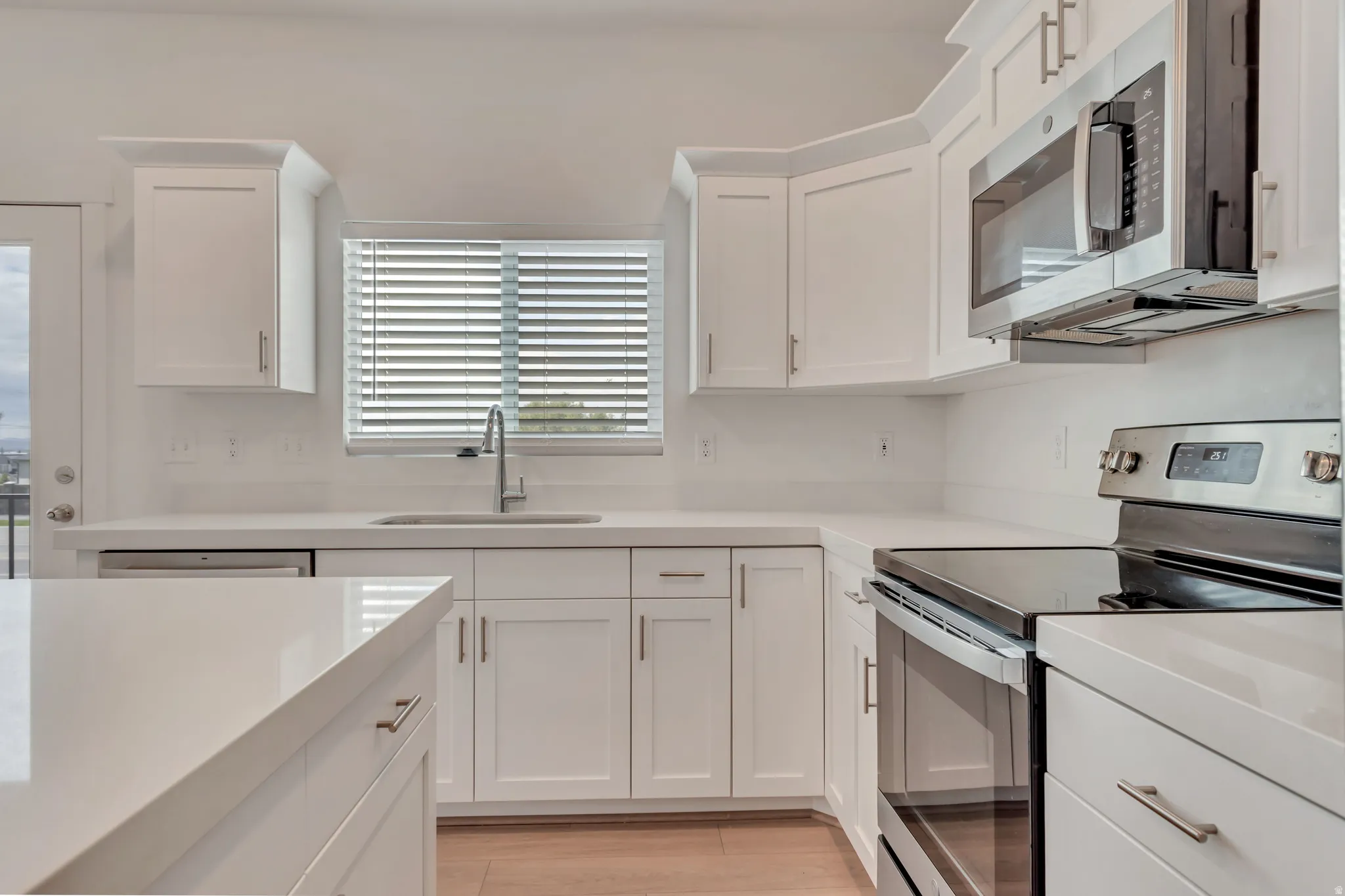 Modern kitchen featuring white cabinetry, light countertops, stainless steel appliances, and wood-finish flooring