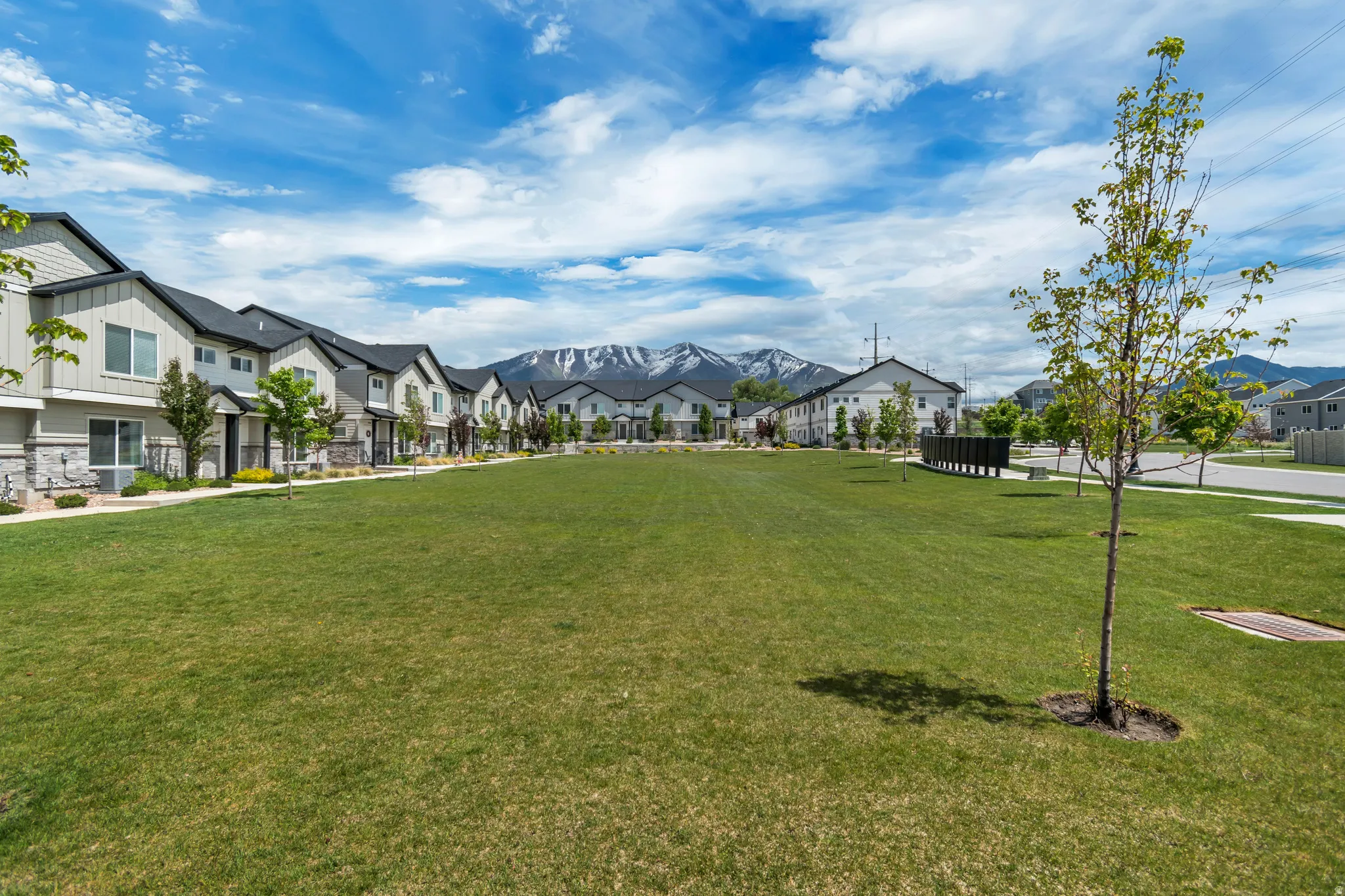 Expansive green space featuring a large lawn area, surrounded by multi-story residential structures with dark roofs and light-colored siding, with mountain scenery in the background