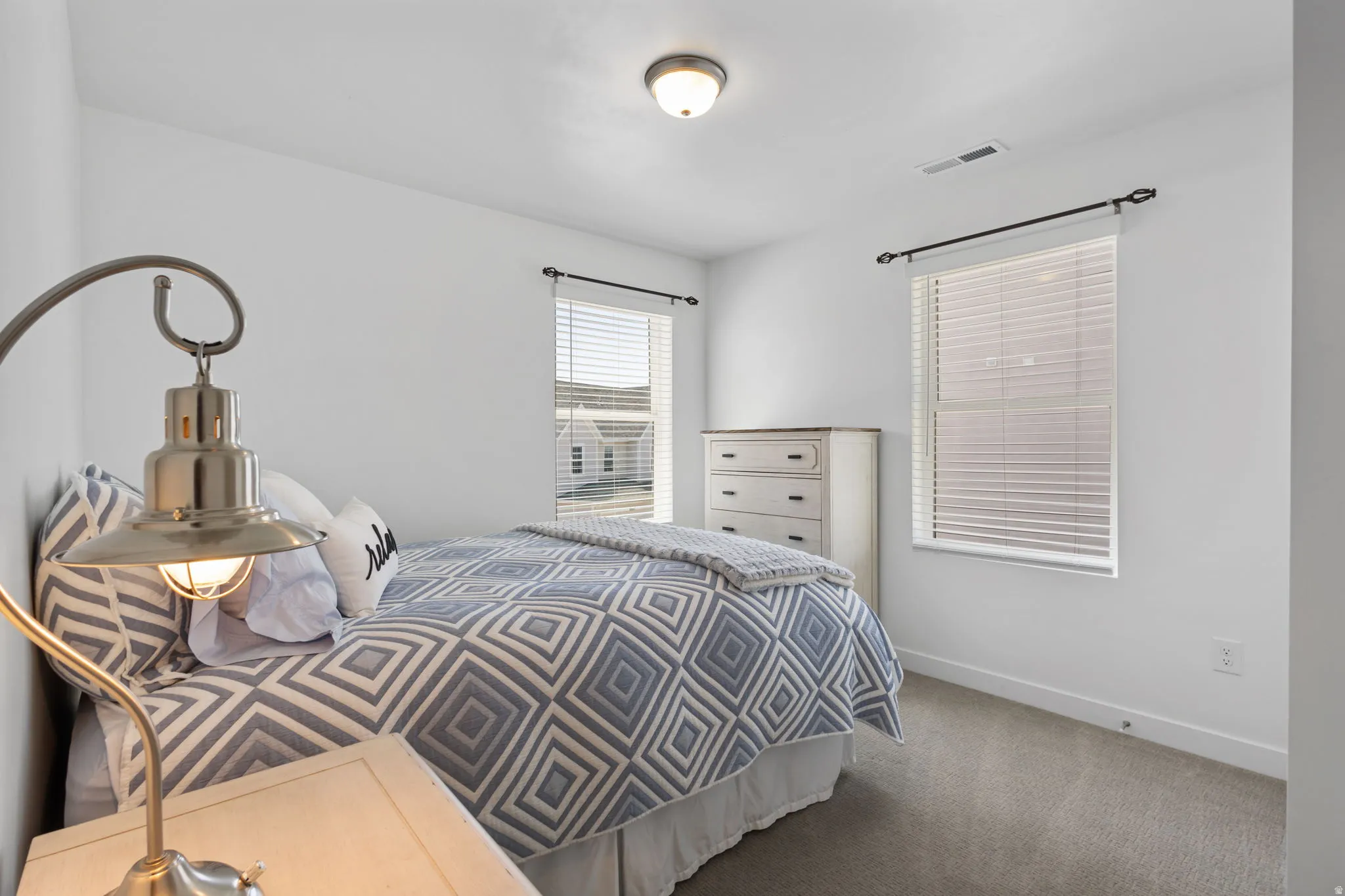 Second bedroom featuring two windows with white blinds, carpet flooring, a ceiling-mounted light fixture, and white wall finishes