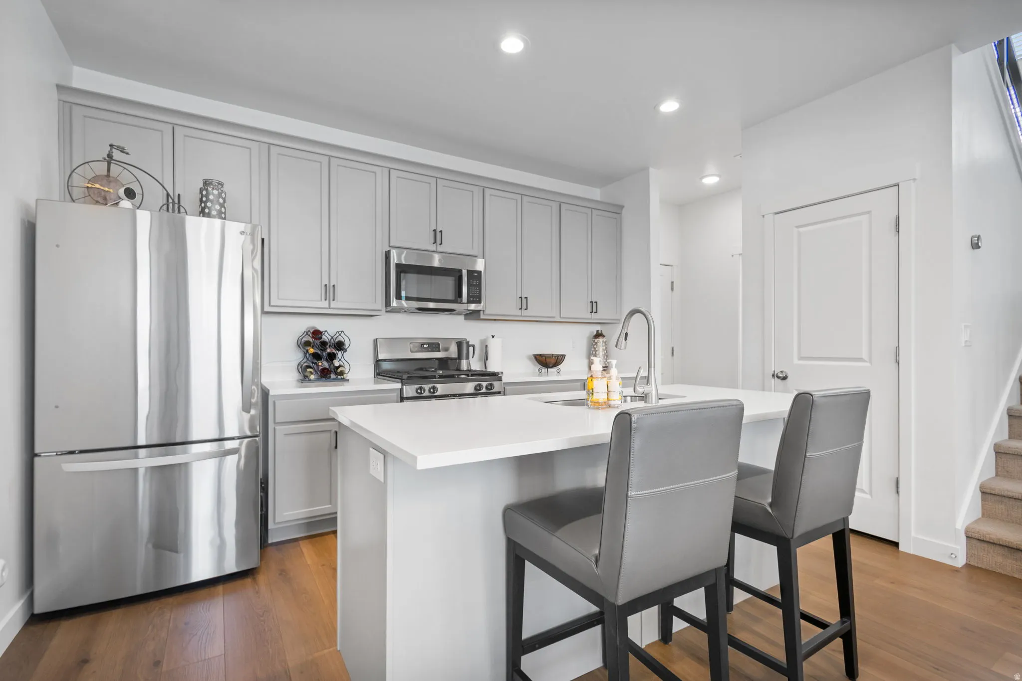 Modern kitchen featuring light gray cabinetry, stainless steel appliances, a white quartz countertop island
