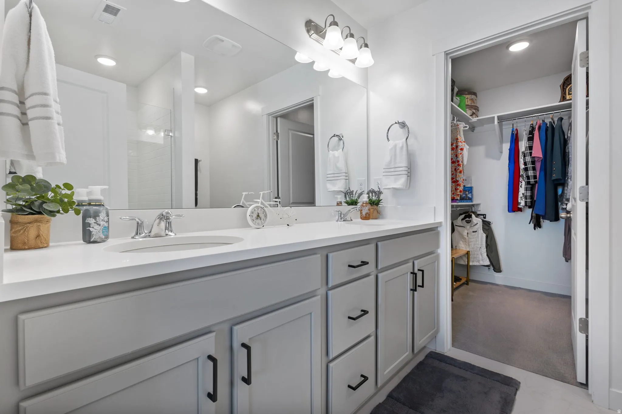 Primary bathroom with double vanity with light gray cabinetry and brushed nickel hardware, featuring a large wall-mounted mirror and overhead lighting