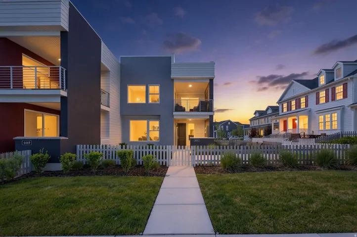Contemporary exterior featuring a modern facade, a covered balcony with metal railings, a covered patio, a central walkway, a white picket fence, and a landscaped lawn.