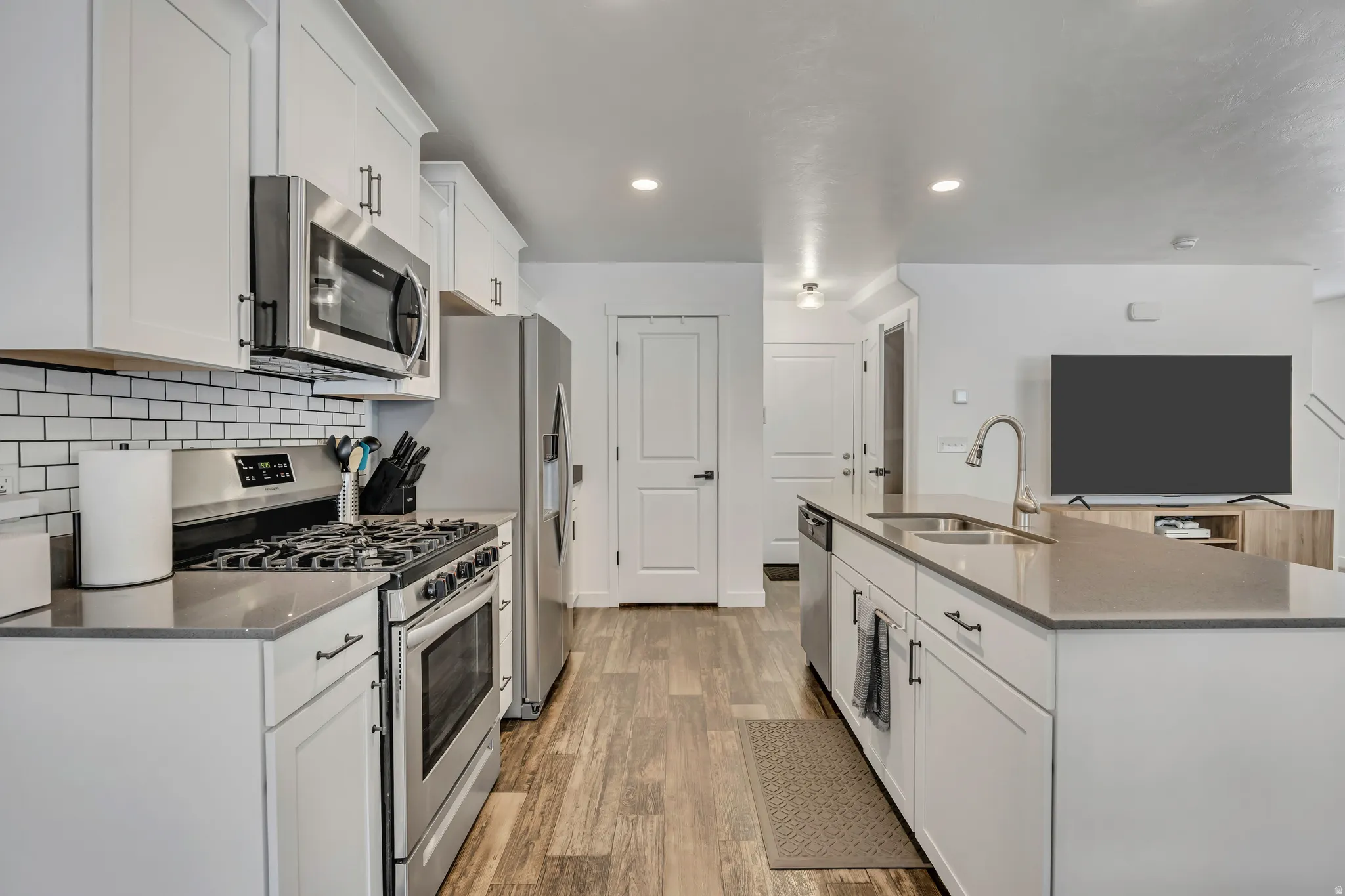 Kitchen featuring white cabinetry, stainless steel appliances, a subway tile backsplash, and wood-finish flooring