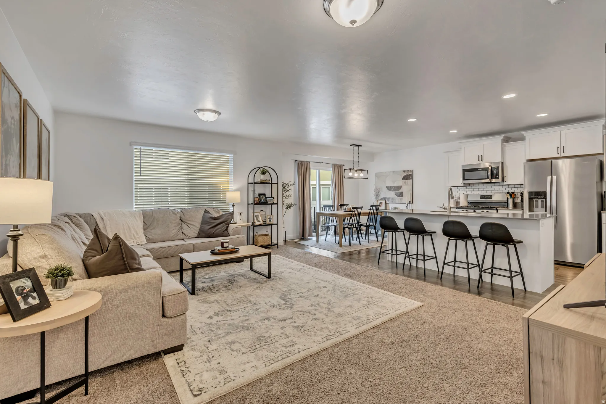 Open-concept living space featuring a bright white kitchen with stainless steel appliances, a spacious central island with bar seating, and white cabinetry