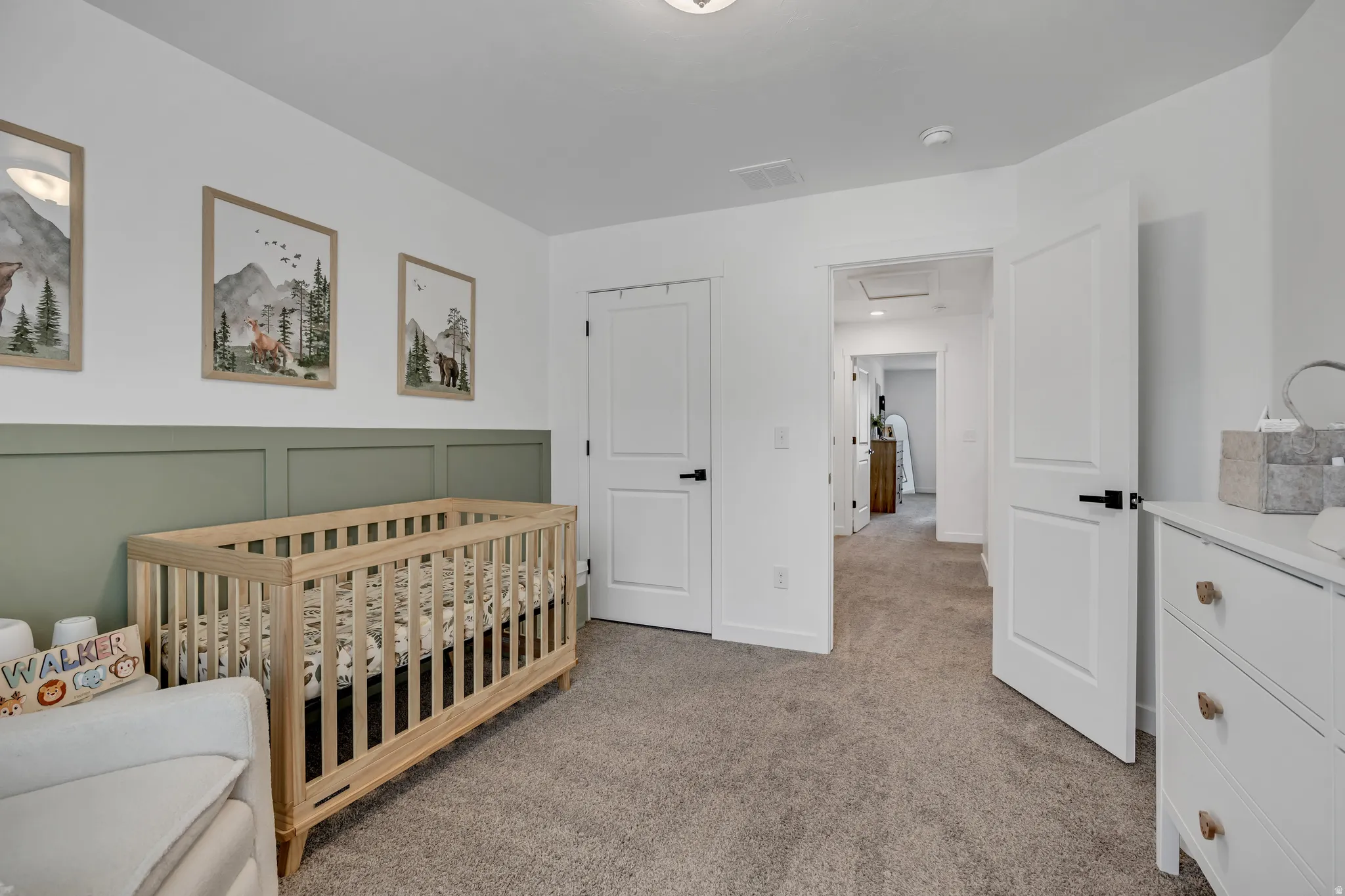 Carpeted room featuring a decorative wainscoting accent wall, white painted walls, and white paneled doors with black hardware