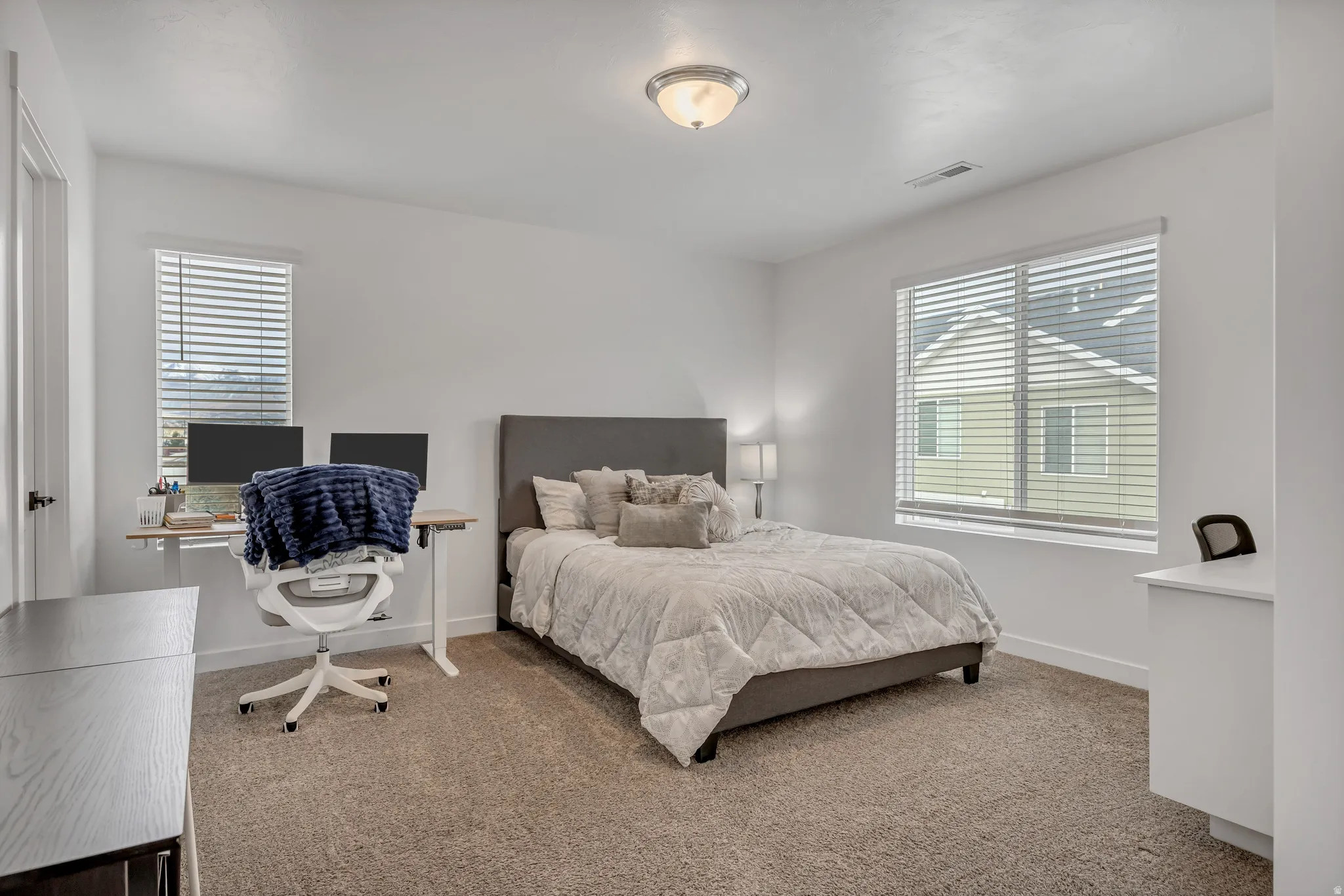 Spacious room featuring neutral carpeting, white walls, and two windows with blinds