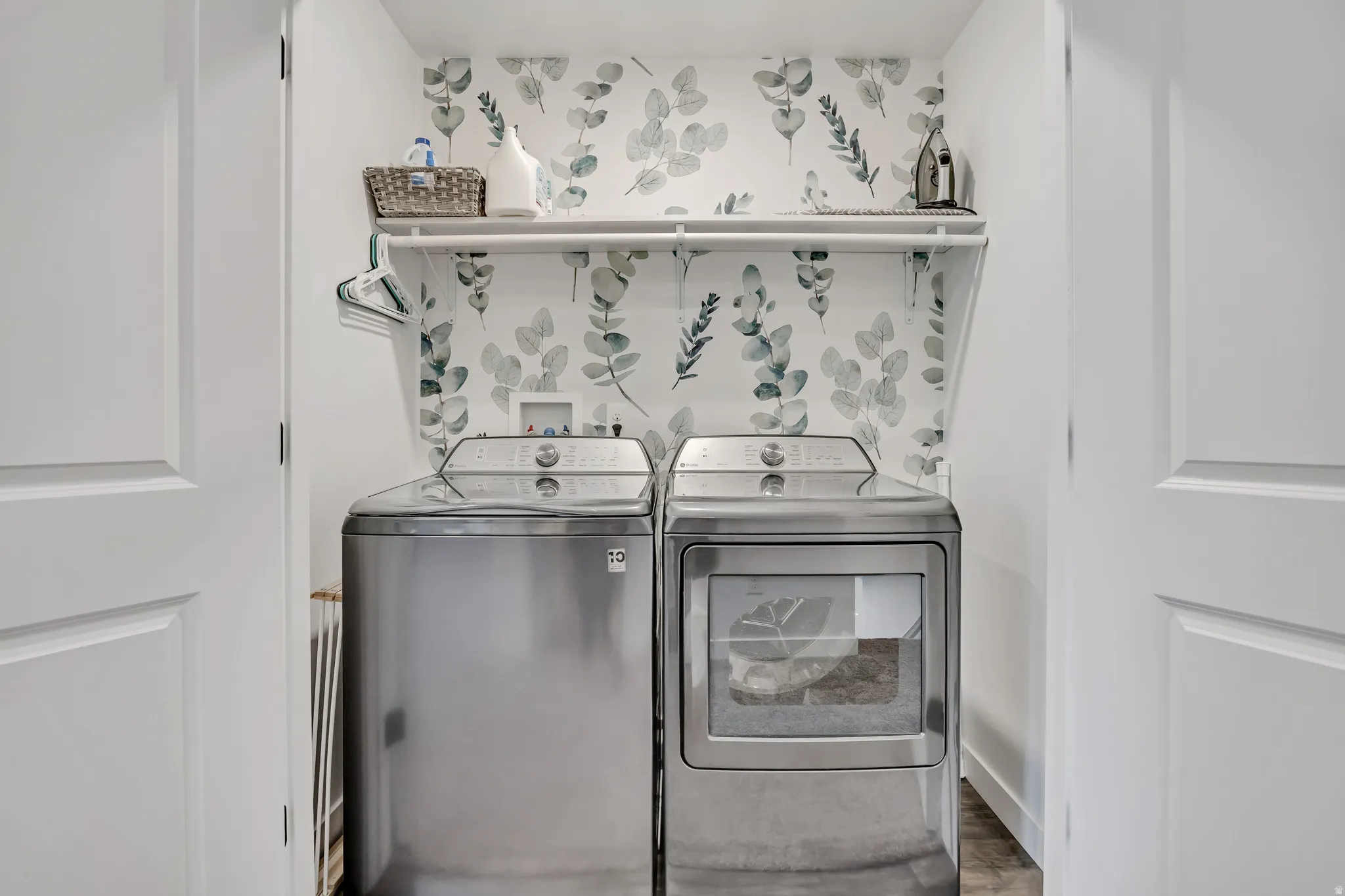 Dedicated laundry area featuring a patterned accent wall, a built-in shelf, and wood-finish flooring