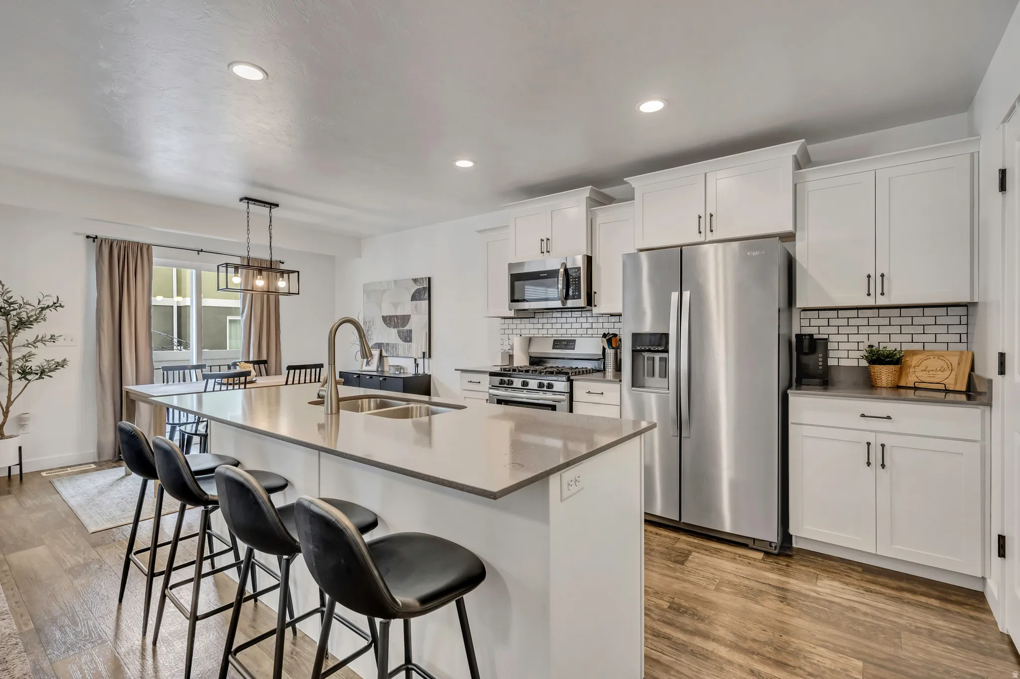 Open-concept kitchen featuring an oversized island with countertop seating, stainless steel appliances, crisp white cabinetry, subway tile backsplash, and wood-finish flooring