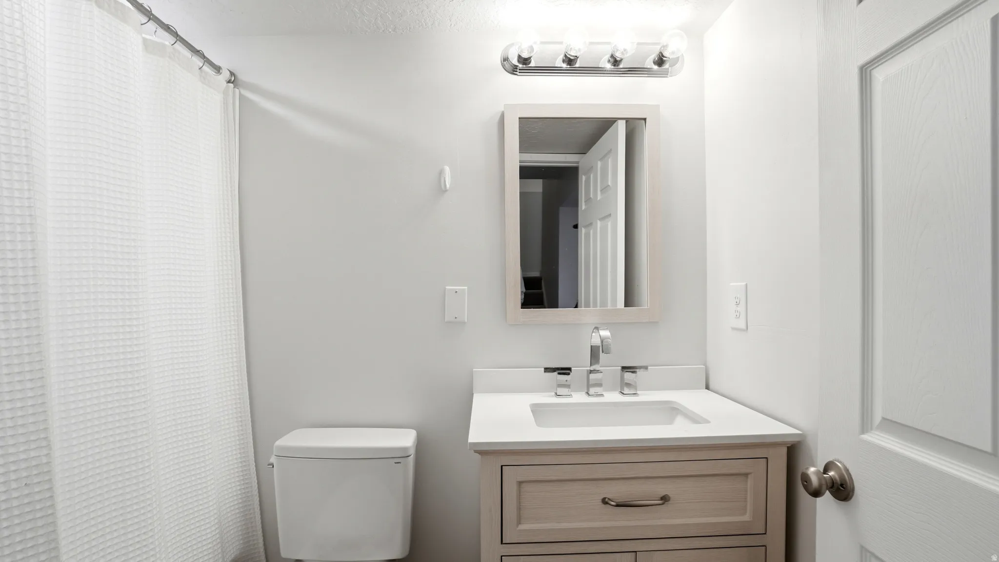 Bathroom featuring a light wood-finish vanity with a white countertop and undermount sink, a framed mirror, and a white toilet