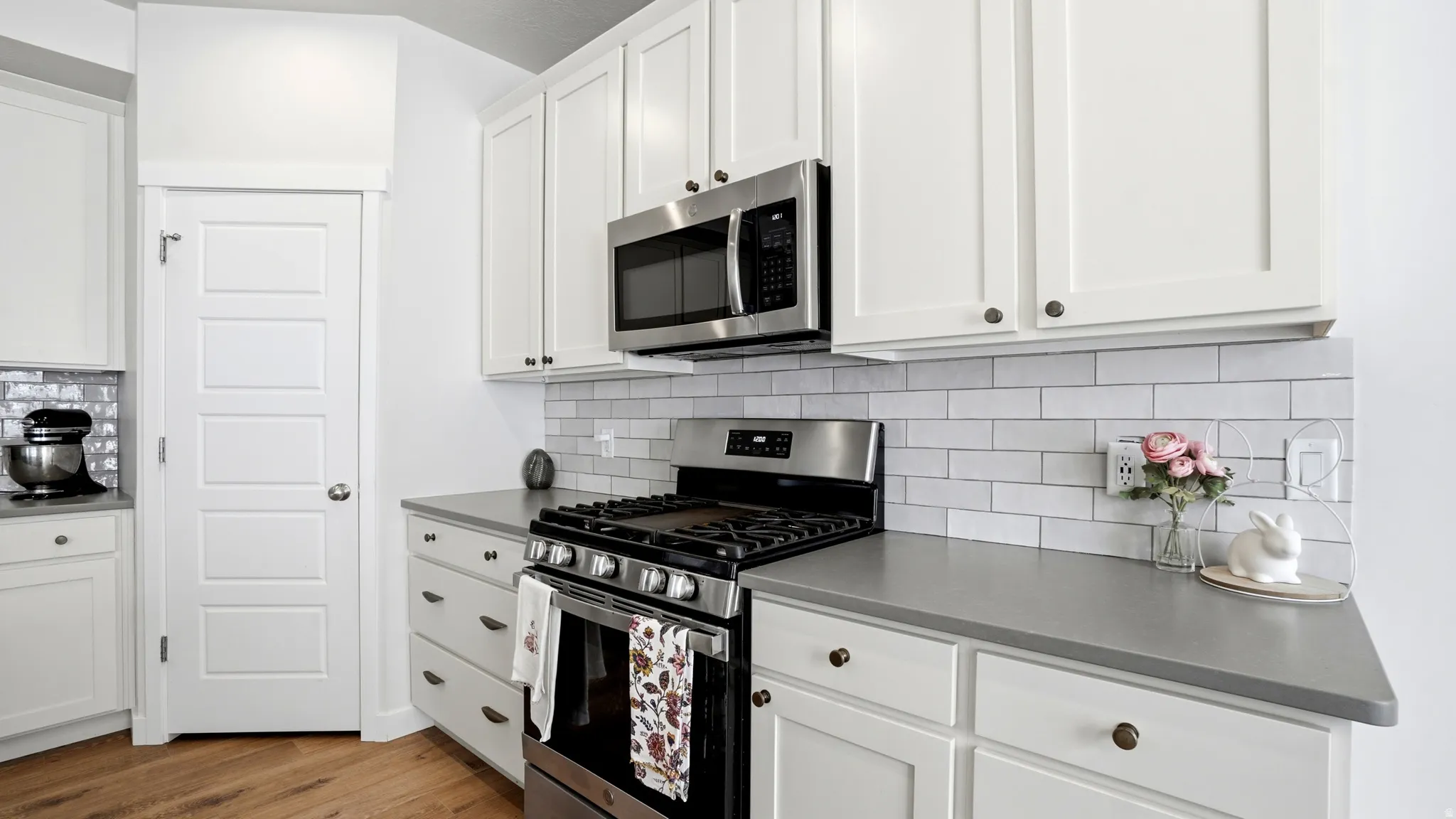 Modern kitchen featuring white shaker cabinetry, stainless steel appliances, a subway tile backsplash, and light wood-finish flooring